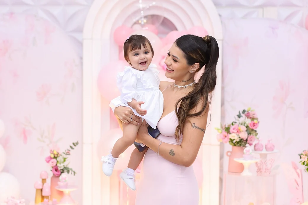 Mãe segurando bebê em festa com decoração rosa